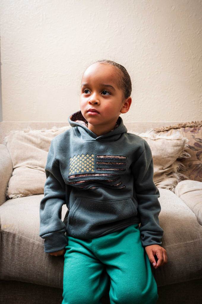 A toddler wearing a green sweatsuit decorated with an American flag.