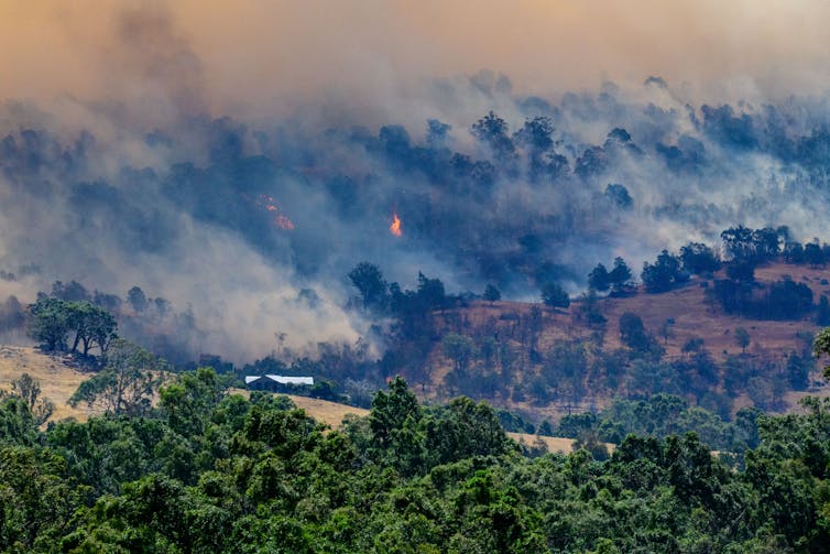 Smoke rises from burning forest on a hillside behind a home near Lockwood, Victoria
