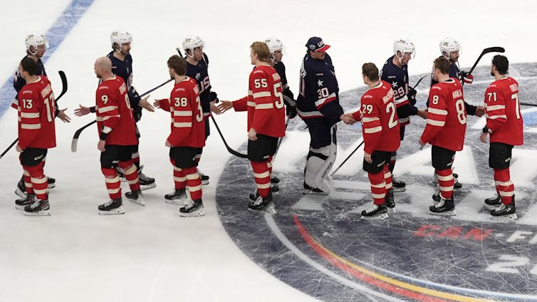 A lineup of hockey players in red shaking the hands of hockey players in blue on an ice rink