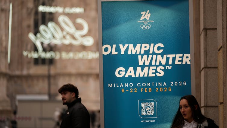 People walk past a sign that says 'Olympic Winter Games Milano Cortina 2026'