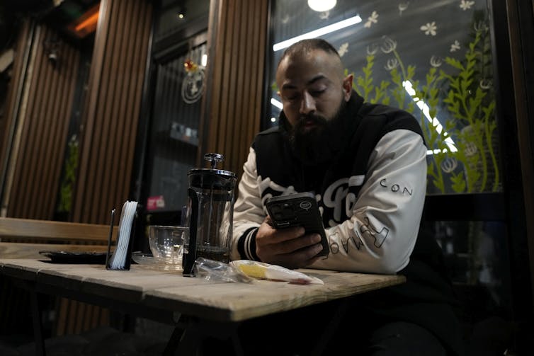 A man looks at his phone at a cafe at night.