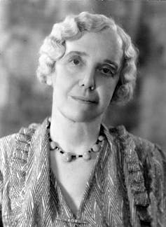 a woman with crimped short grey hair and a beaded necklace