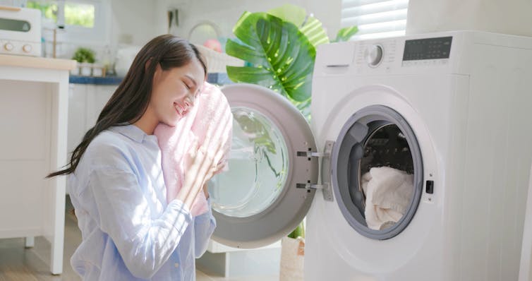 A person takes clothes out of a washing machine and holds them to her face.
