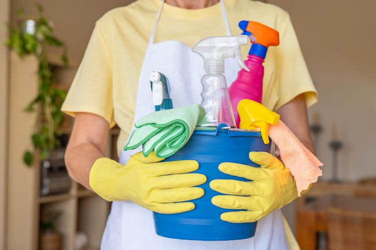 A person wearing yellow gloves holds a bucket of cleaning supplies.