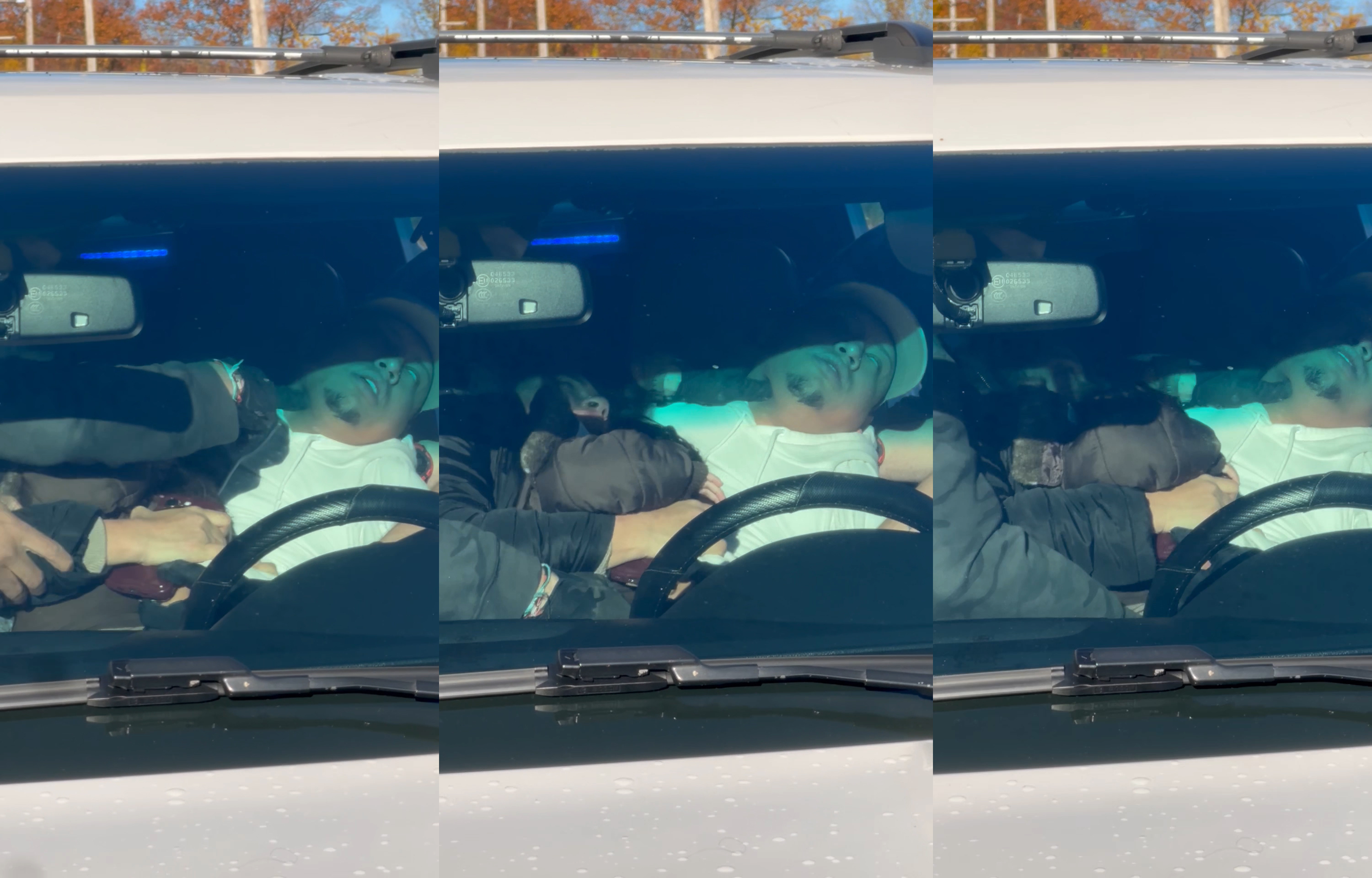 A man wearing a white shirt and baseball hat convulses in the driver’s seat of a car while a black-gloved hand presses into his neck.