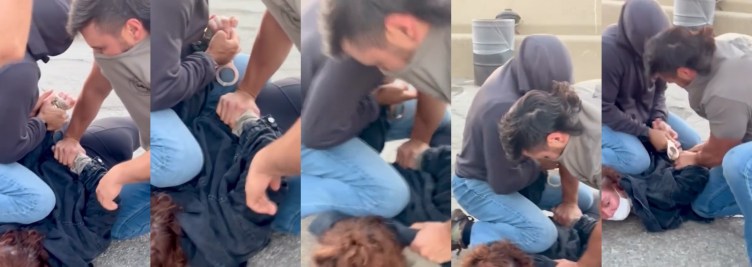 A woman wearing a white mask and blue jacket is pinned to the ground and handcuffed by two men wearing blue jeans and covering their faces with their shirts.