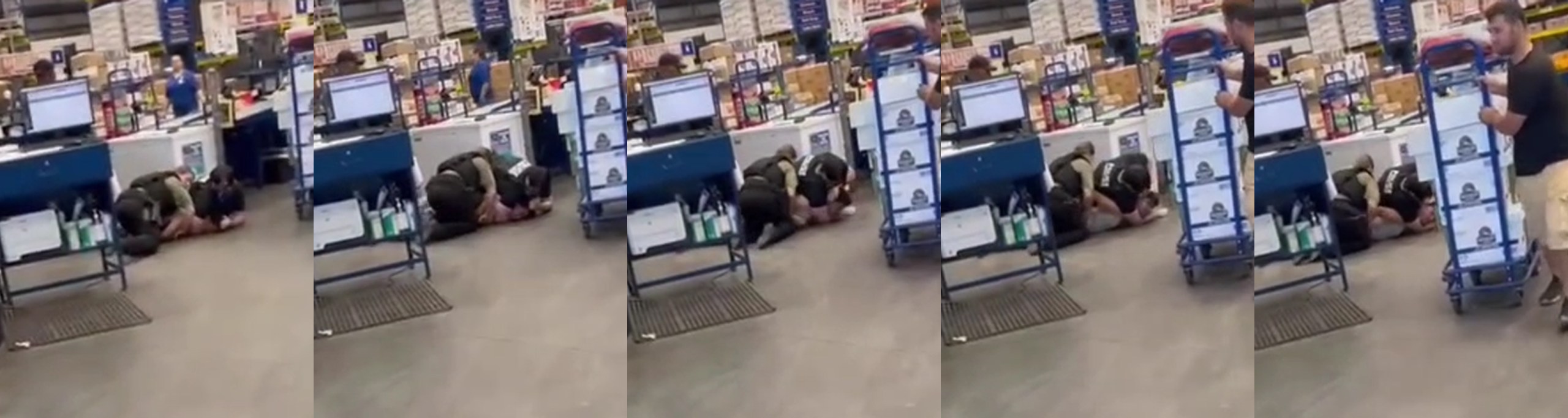 Two men, wearing black armored vests, pin and choke a young man on the ground of a large warehouse store.