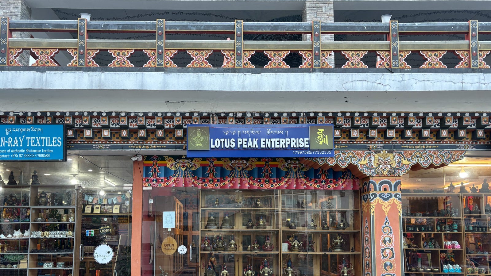 A storefront displaying various crafts and artifacts, with a colorful sign reading "Lotus Peak Enterprise." Intricate architectural details above.