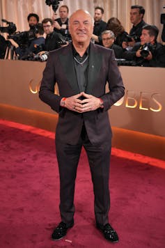 A man in a suit smiling broadly as photographers stand behind.