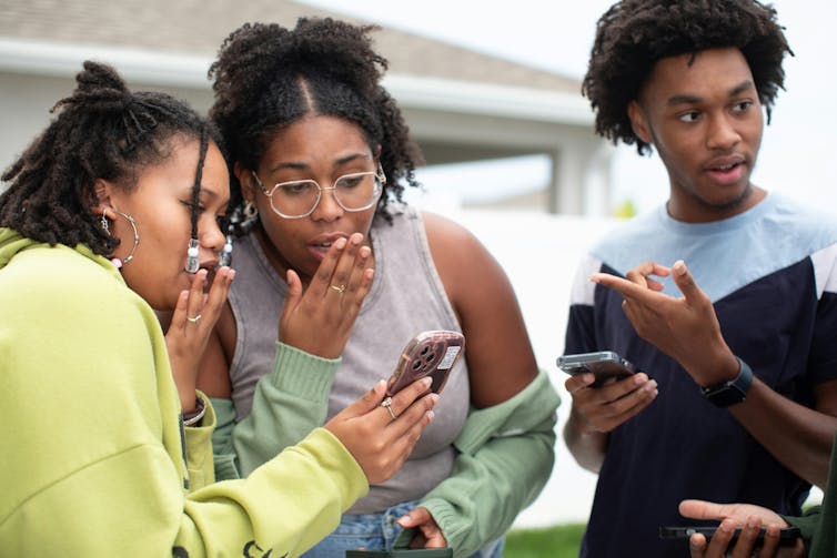 Three Black people holding their phones and discussing.