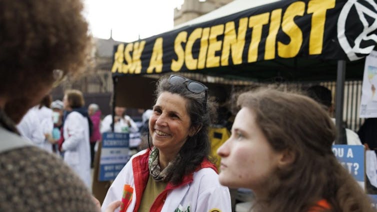 scientists answering questions from public at outside protest, ask a scientist banner in background