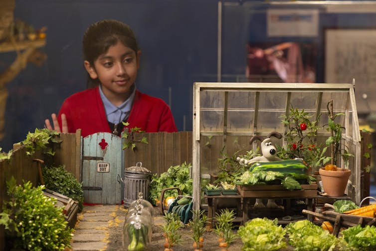 A young girl in a red cardigan looking at a a museum exhibit.