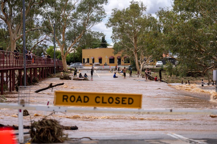 Alice springs flood, people watching water going over flooded bridge and road closed sign in foreground.