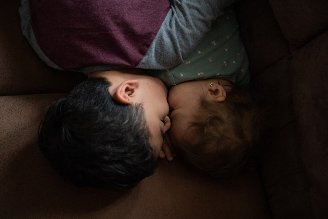 Two young children in pajamas, lying with their faces pressed together.