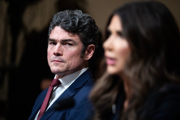 A man wearing a suit looks past the camera with a furrowed brow.