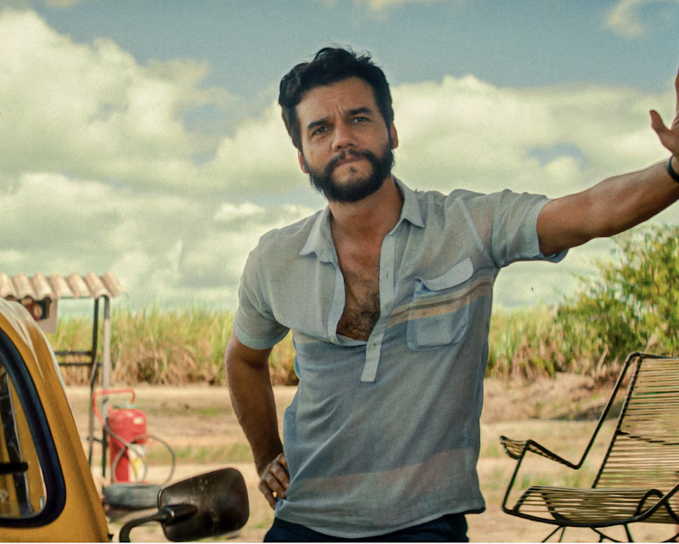 Very handsome man with black hair and beard leaning against a wall.