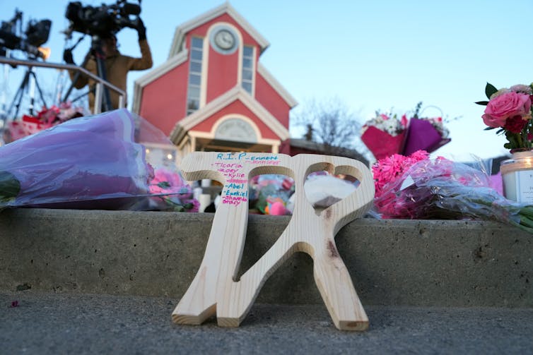 A wooden carving with names inscribed on it sits on a road.