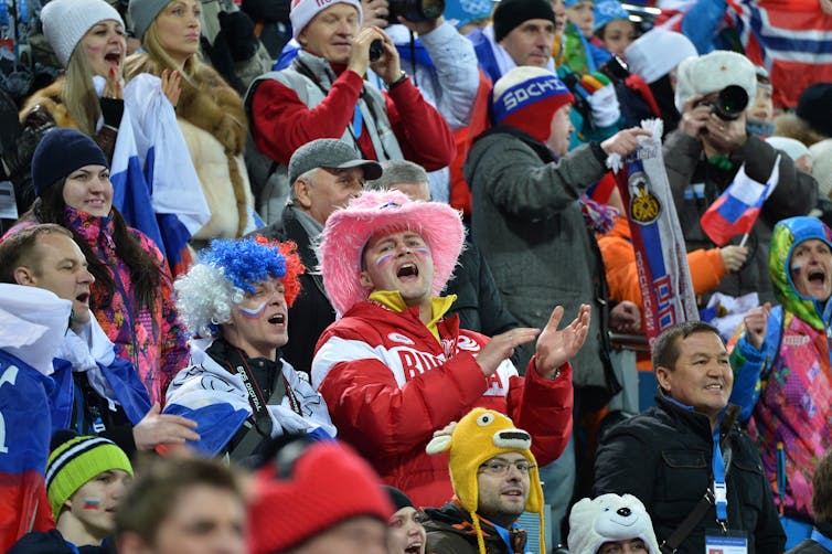 A stand full of cheering fans wearing winter gear and Russian colors.