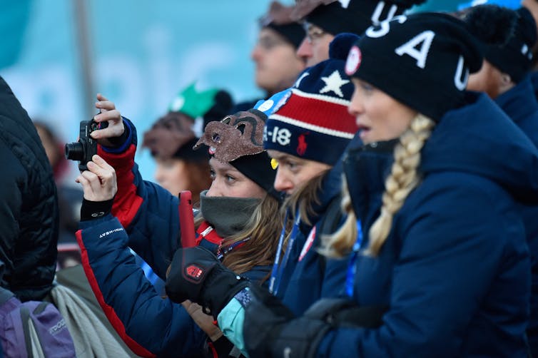 A group of athletes wearing thick jackets, hats and face coverings take a picture together.