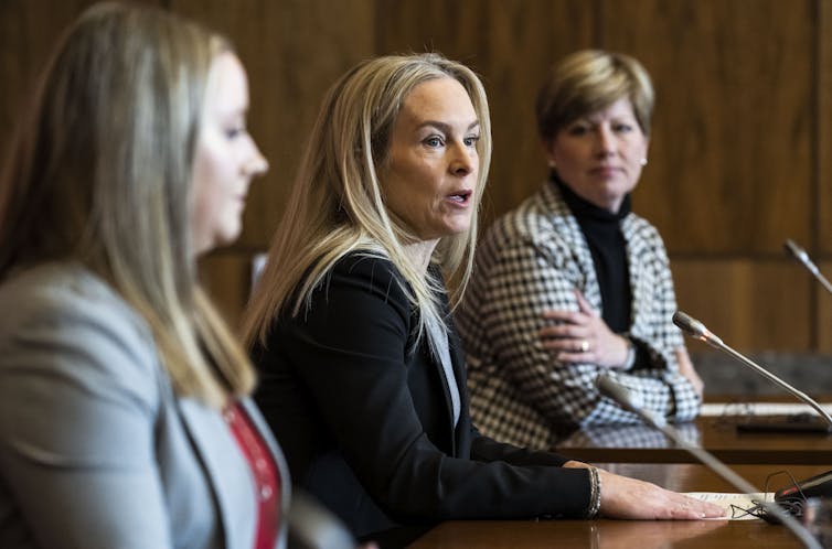 Three women sitting behind a podium during a conference.