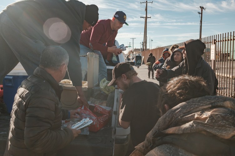 Two men stand in a truck bed and hand out food to a line of people along a sidewalk in Albuquerque, New Mexico.