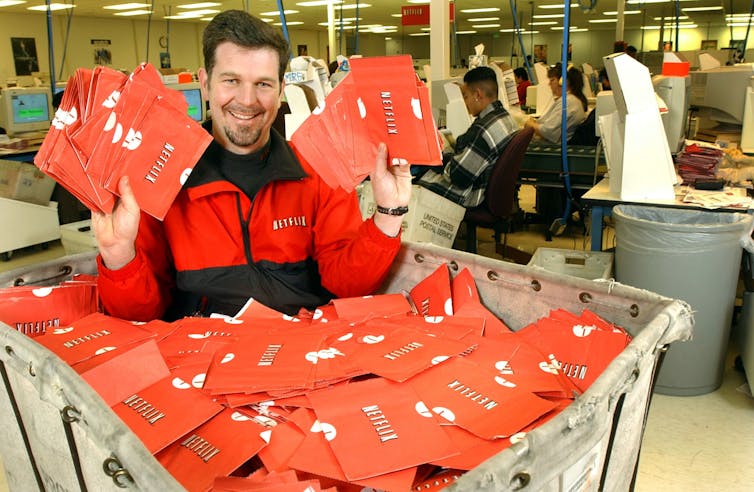 Netflix.com Chief Executive Officer Reed Hastings sits in a cart full of ready-to-be-shipped DVDs