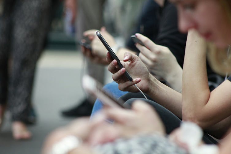 Closeup of people's hands as they scroll on their phones while sitting on a bench