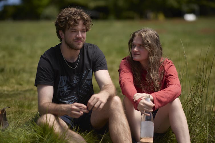 Production image: Dee and Darcy sit in a grassy field.