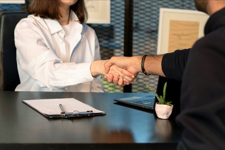 Two people shake hands across a desk