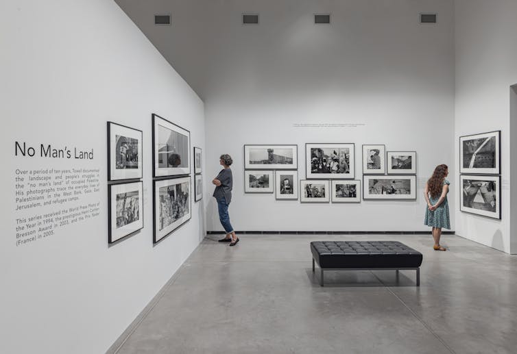 Installation view of two women looking at photographs in an art gallery
