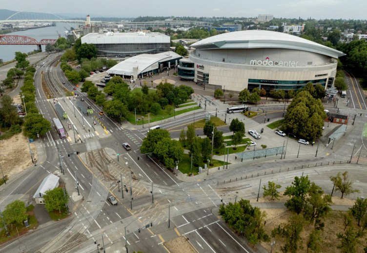Aerial view of the area surrounding a large building with the sign Moda Center written on it. Roads and trees surround the building.