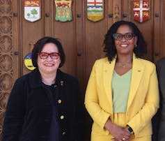 Two women in business dress pose for a photo.