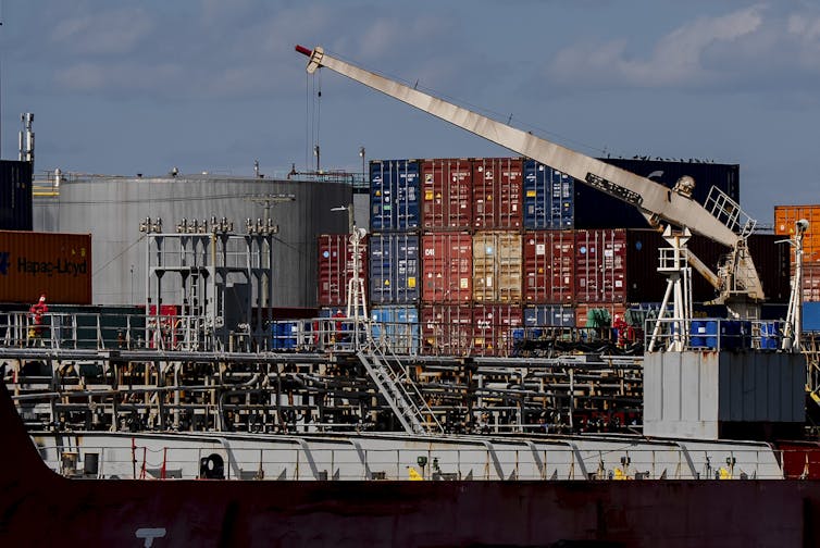 A cargo ship docked in front of a port stacked high with shipping containers