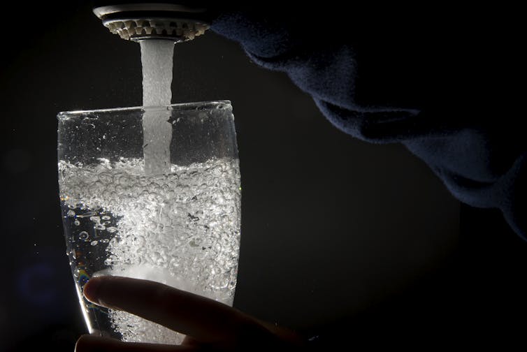 A running faucet filling a glass with water, with a black background.