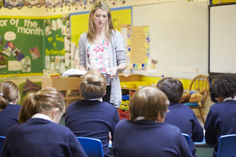 A teacher speaks to seated pupils.