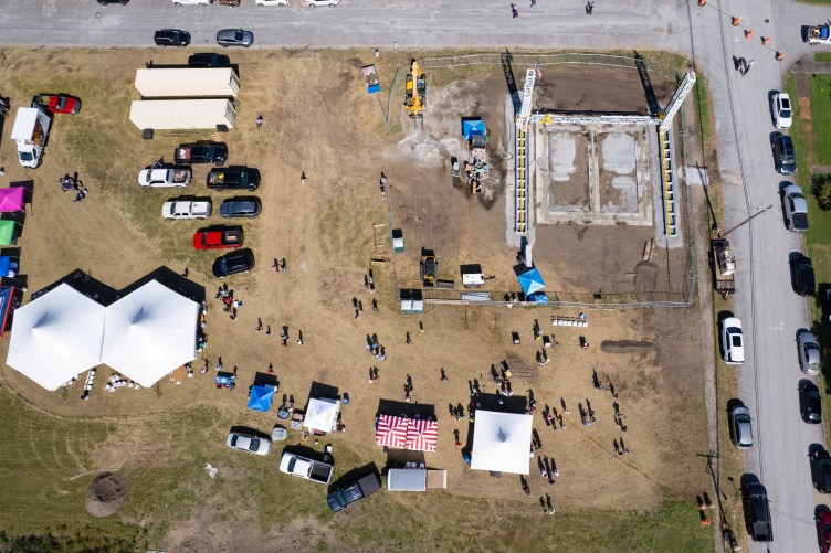An overview of a field with tents, cars, people and a huge structure that is a 3D printer.