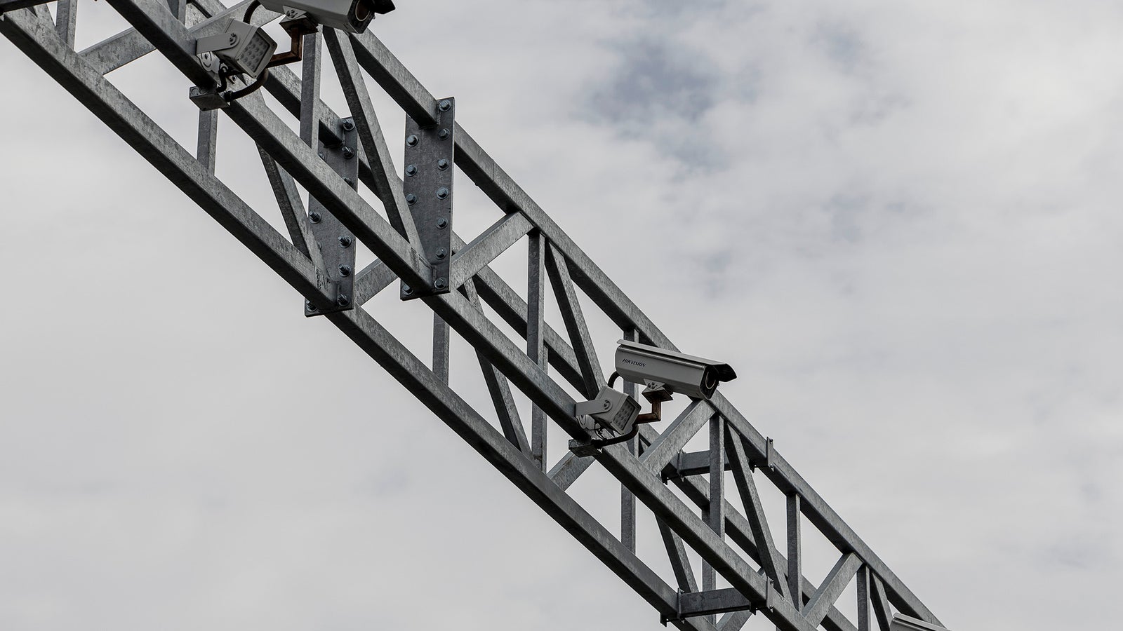 A row of security cameras mounted on a metal framework against a cloudy sky.