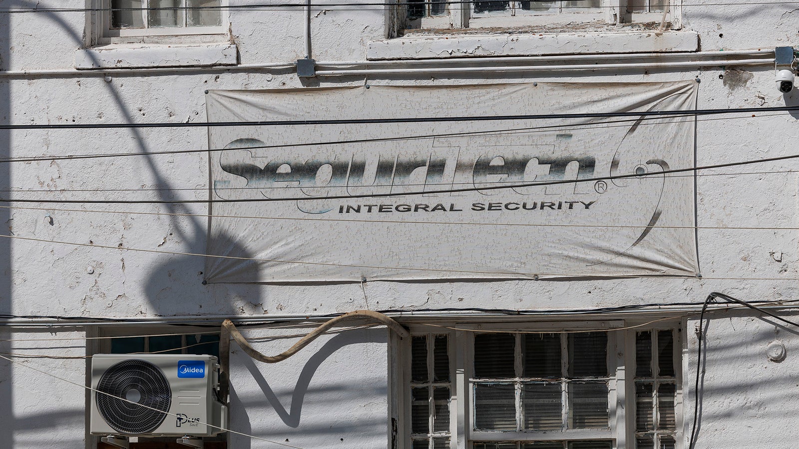 A weathered building features a large banner for "Seguritech Integral Security" and an air conditioning unit.