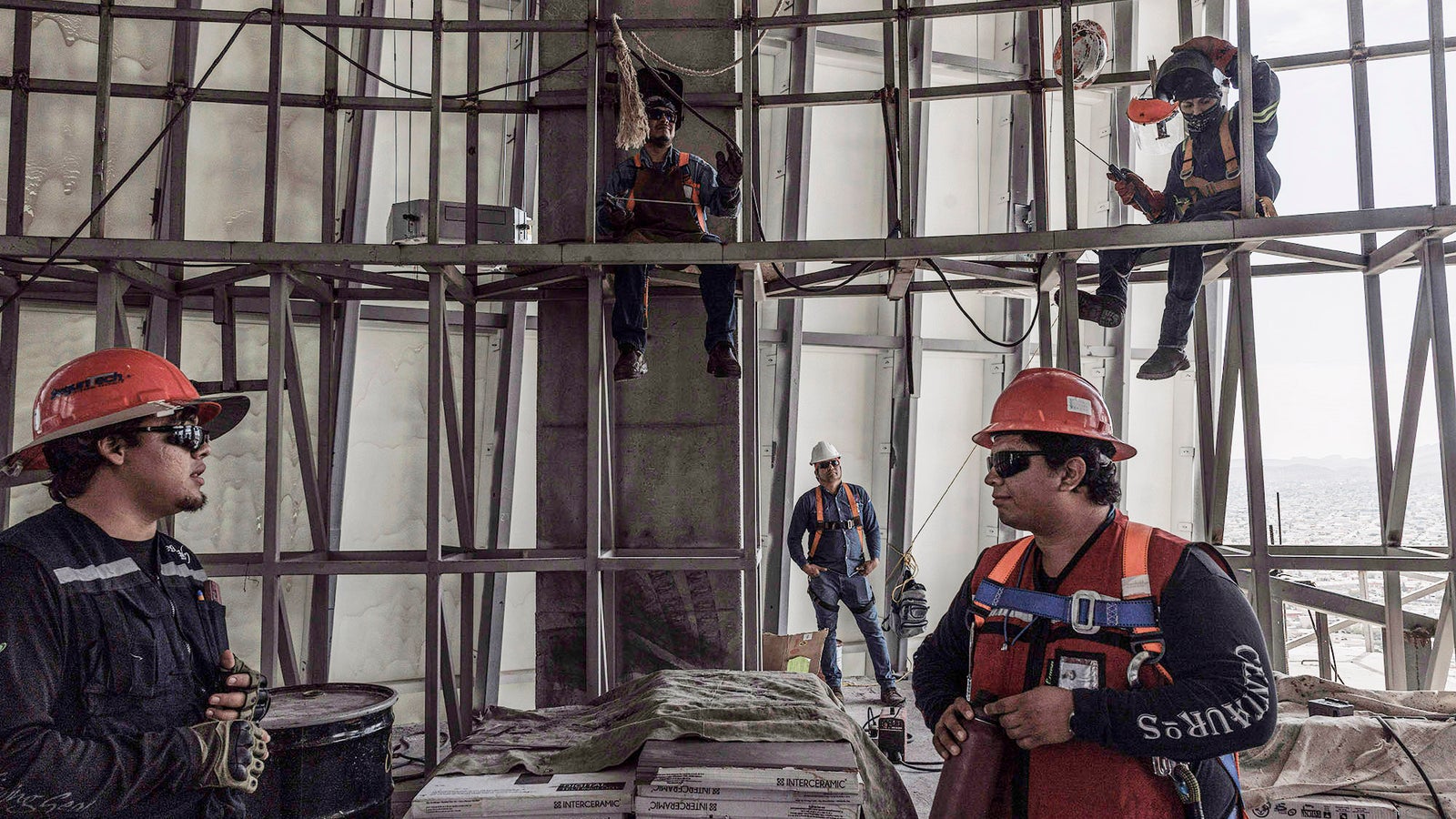 Construction workers wearing safety helmets and gear are engaged in conversation on a building site, with scaffolding in view.