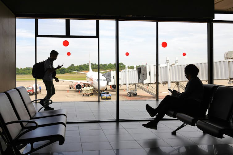 Two silhouetted people seen at an airport with bags.