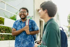 Two young men in discussion, with one laughing and the other in profile listening and also smiling.