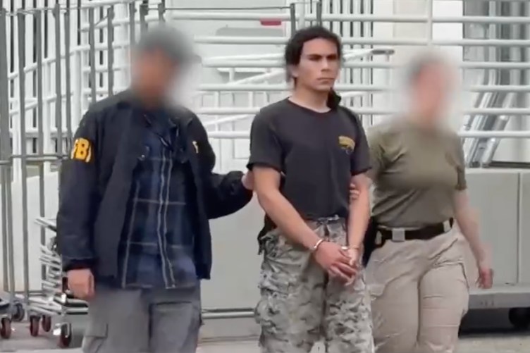 Two agents with blurred faces, one of whom has an FBI jacket on, escort a man in handcuffs.