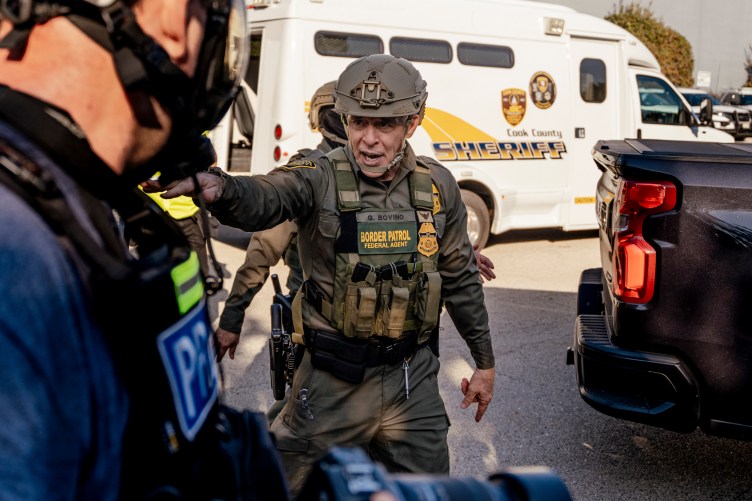 Gregory Bovino, wearing a full camouflage uniform and a helmet, points and speaks.