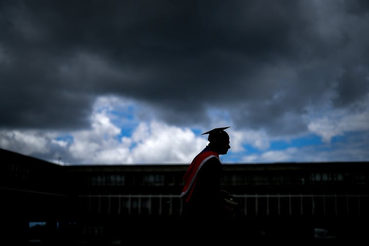 A graduate in cap and gown silhouetted against a dark sky.