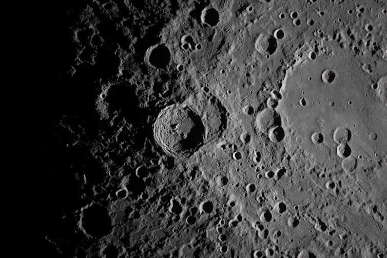 Close-up, grey-coloured, image of the moon's cratered surface.