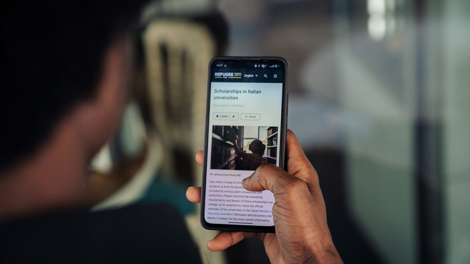 A person holds a smartphone displaying information about scholarships in Italian universities.