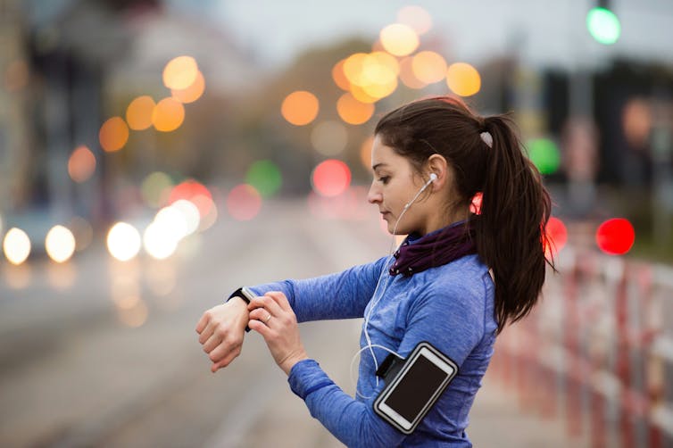 a woman uses a smartwatch on her wrist,  a smartphone is on her arm