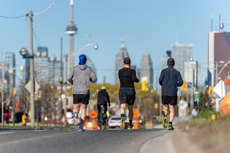 Three people run along a path together, the CN tower and tall buildings seen in the background