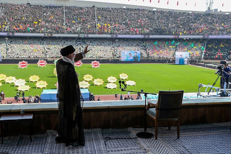 A man waves to a large crowd in an athletics stadium