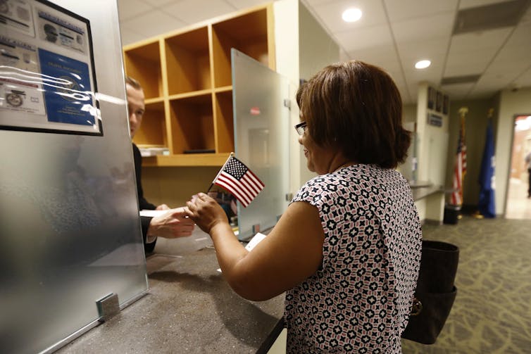 A woman accepts a small American flag handed to her from a man across a counter.